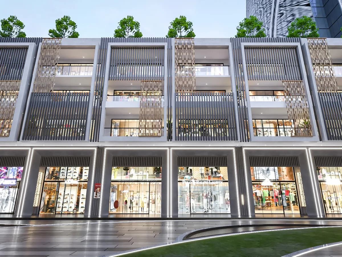 Render of the India World Mart shop-cum-office block at dusk: lit showroom fronts at ground level below three floors of glazed offices framed by grey fins and gold screens.